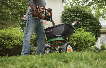 Person applying Ortho BugClear insect killer to spreader for outdoor lawn pest control in garden care setting