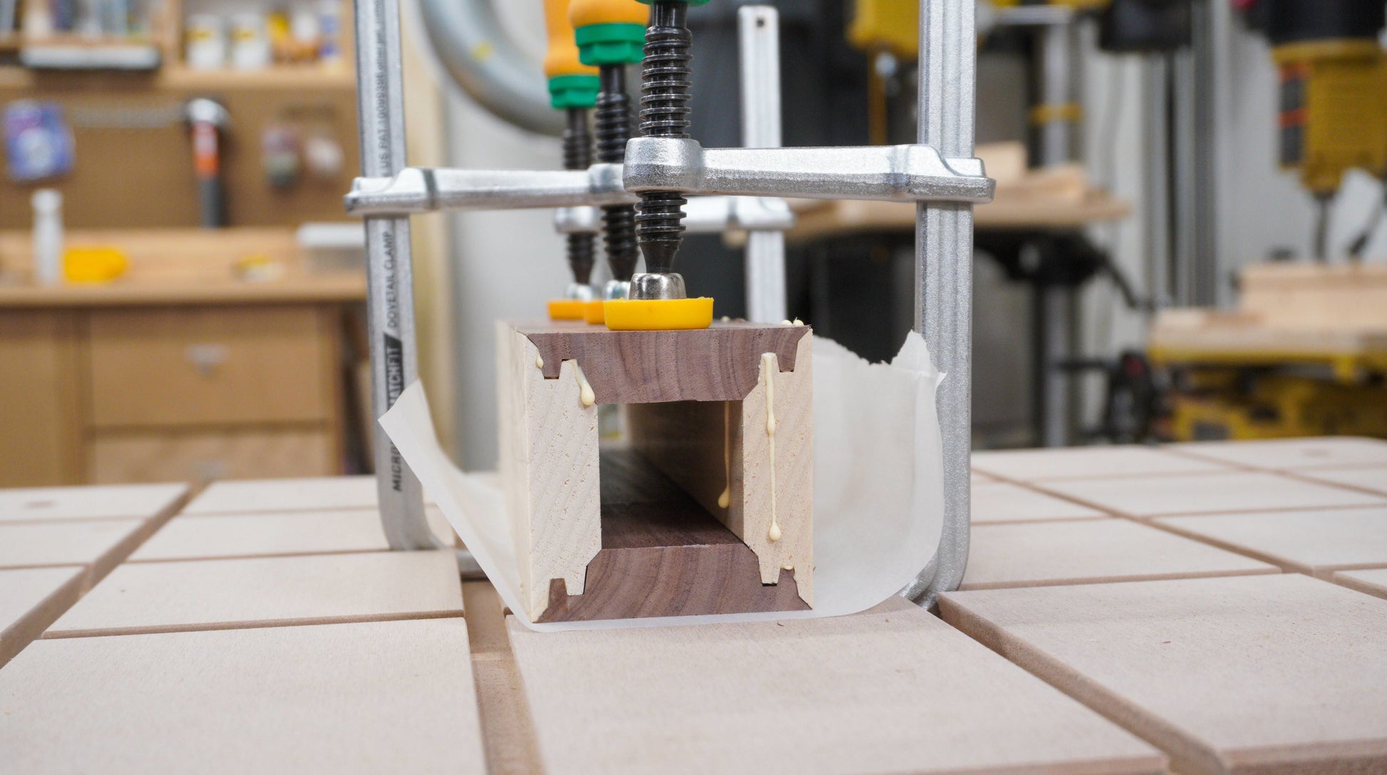 Woodworking clamp securing glued mitered wood joint on workbench in a workshop setting for precision tools use