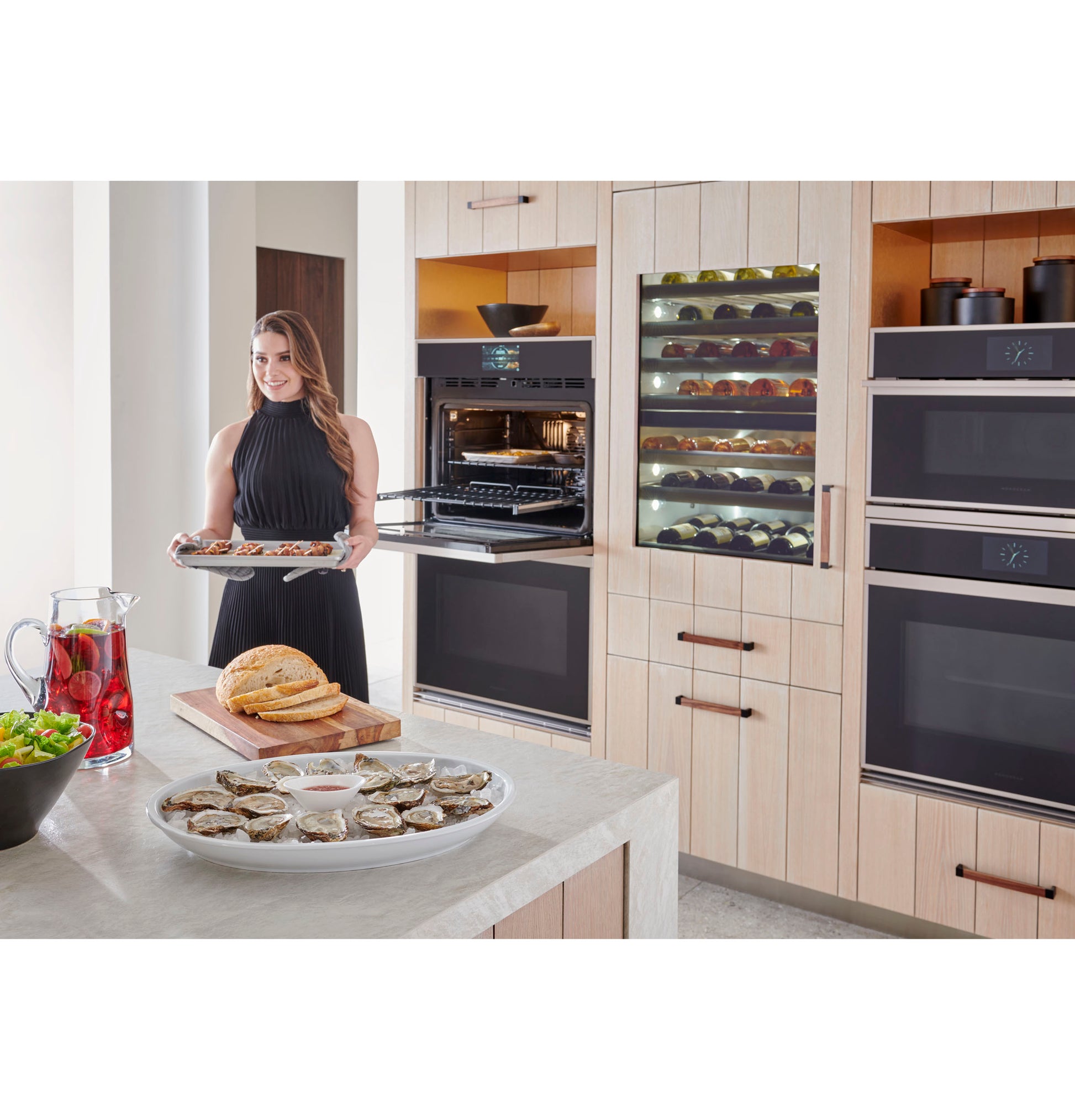 Woman placing tray into minimalist double wall oven in modern kitchen with wine cooler and wooden cabinetry