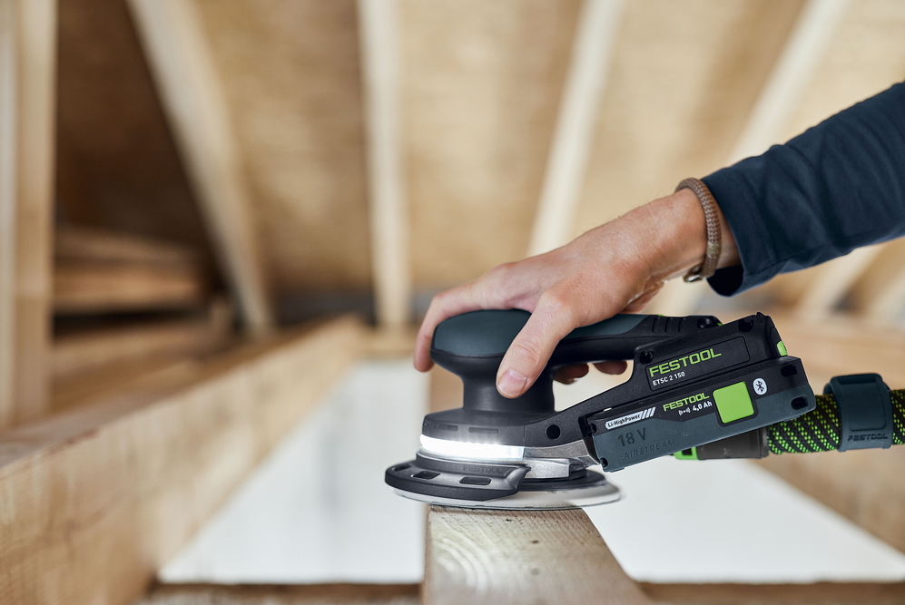 Hand operating cordless random orbit sander on wood beam in woodworking and power tools setting