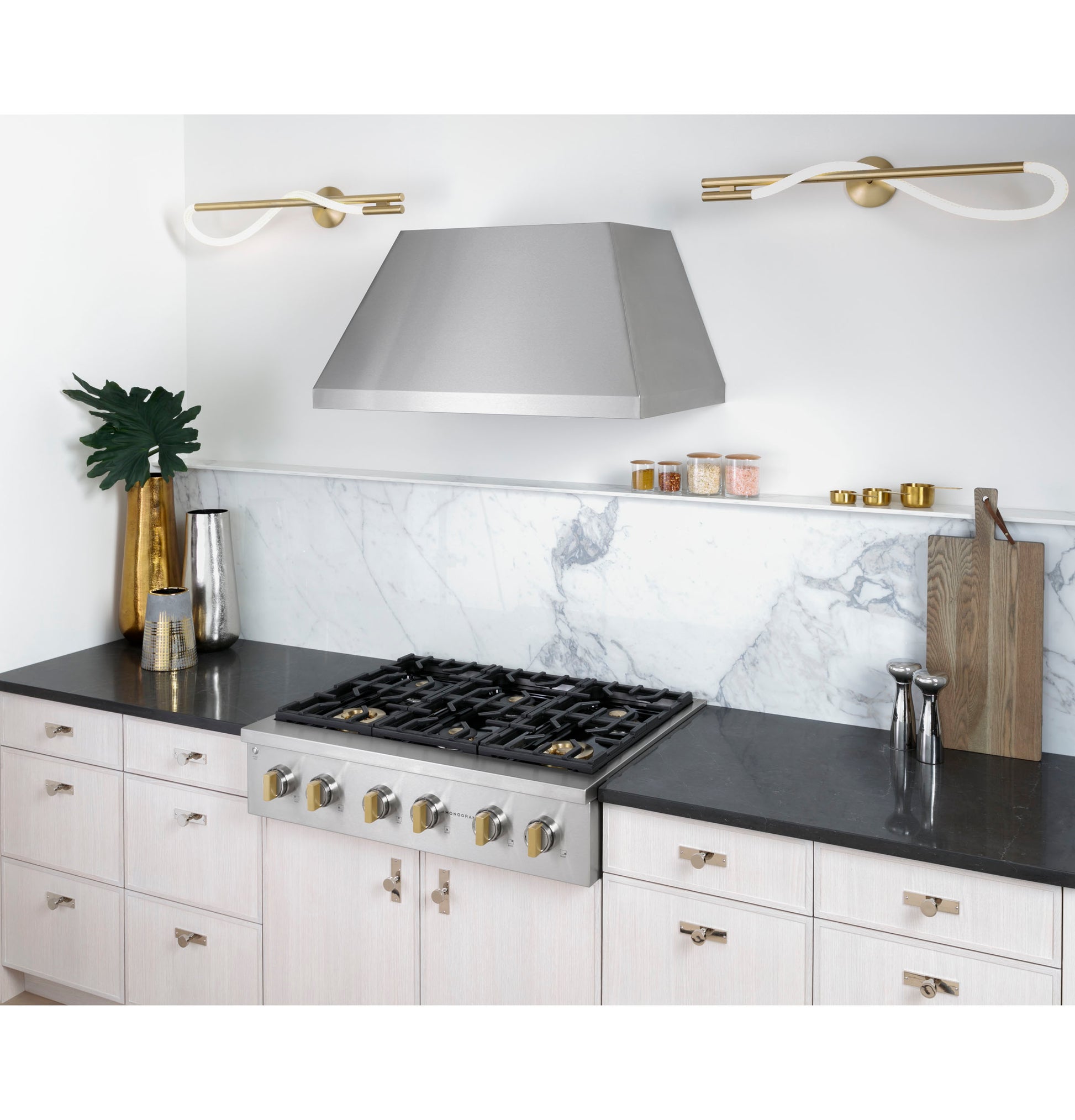 Modern kitchen with stainless steel range hood above gas cooktop, white marble backsplash, and light wood cabinetry in appliances collection