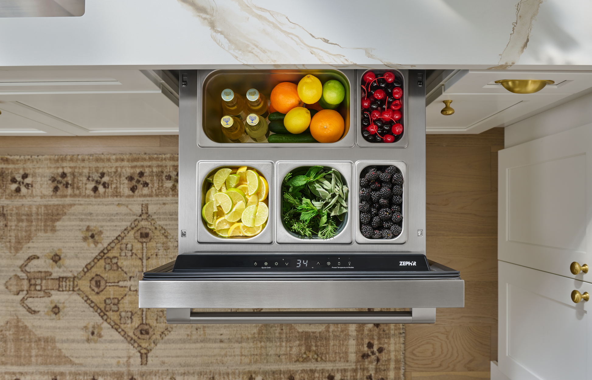 Under-counter stainless steel refrigerator drawer with fresh citrus, berries, herbs, and bottled beverages in kitchen setting