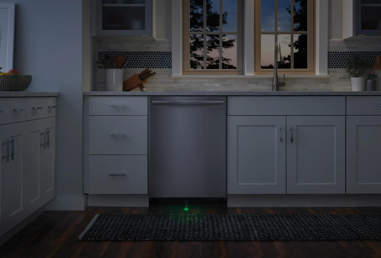 Built-in stainless steel dishwasher with sleek design integrated into white kitchen cabinetry at dusk.