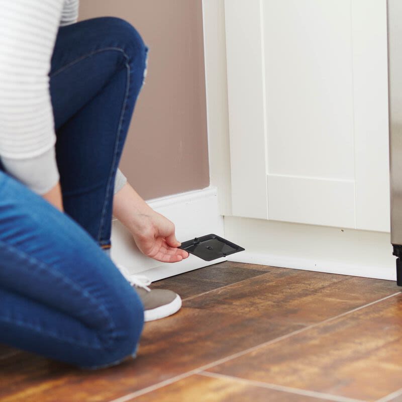Person placing black Tomcat glue trap with enhanced stickiness on kitchen floor near white cabinetry for pest control