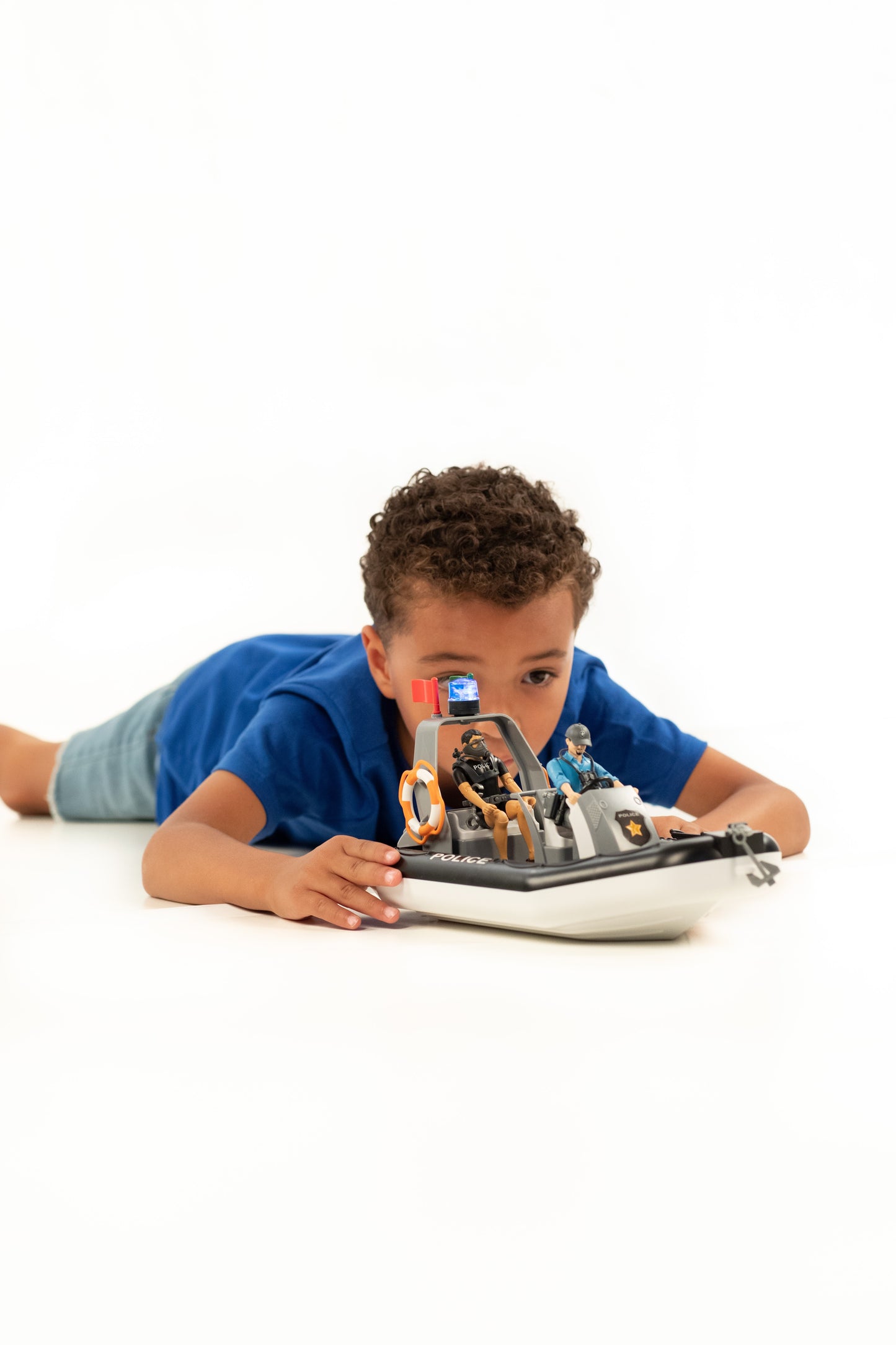 Young boy playing with detailed police boat featuring rotating beacon light and two officers on white background