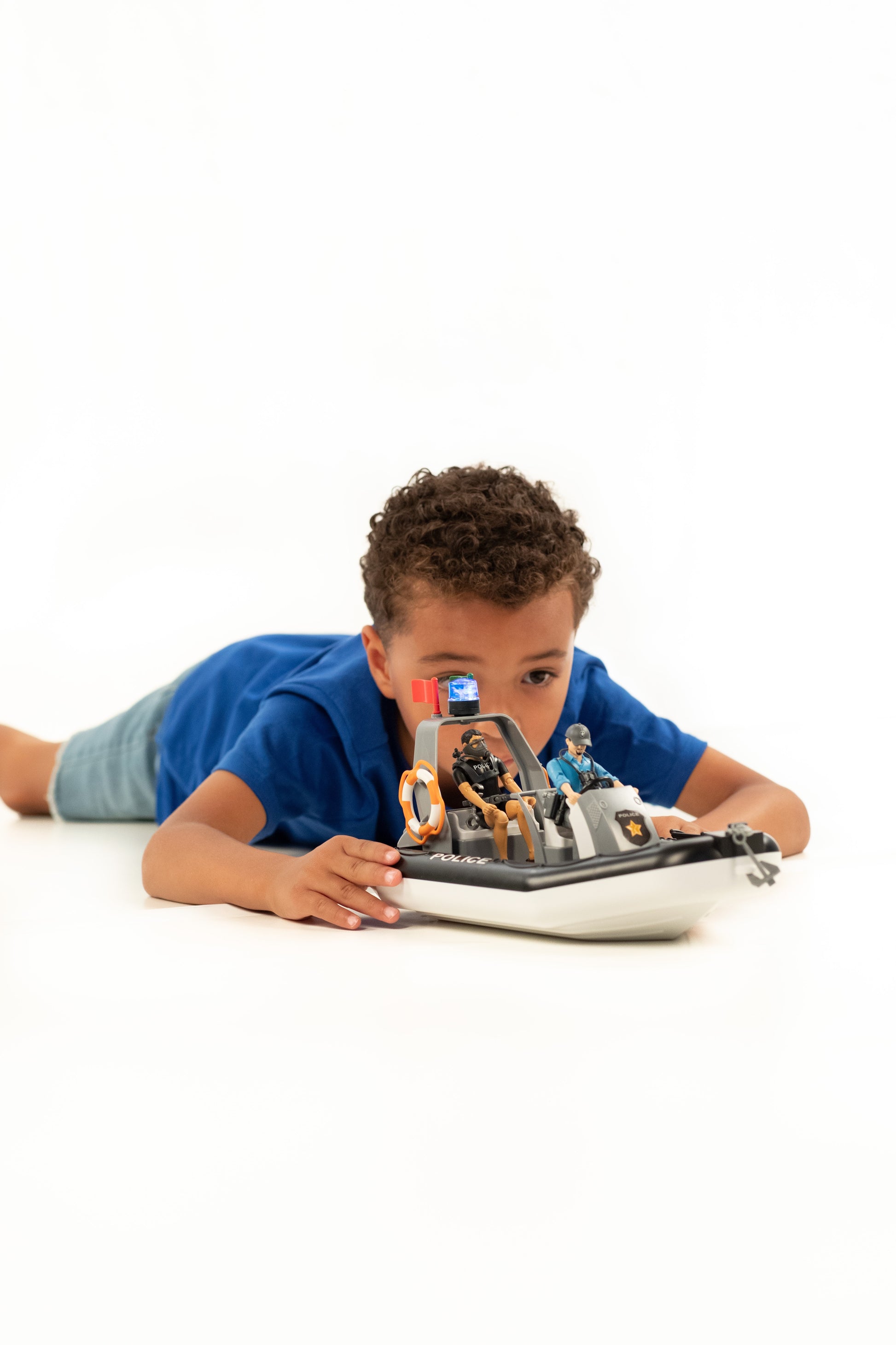Young boy playing with detailed police boat featuring rotating beacon light and two officers on white background