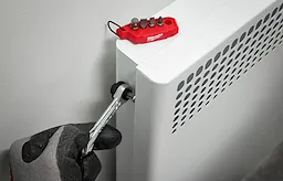 Gloved hand using mini ratchet with red bit holder to tighten radiator valve for home improvement tasks