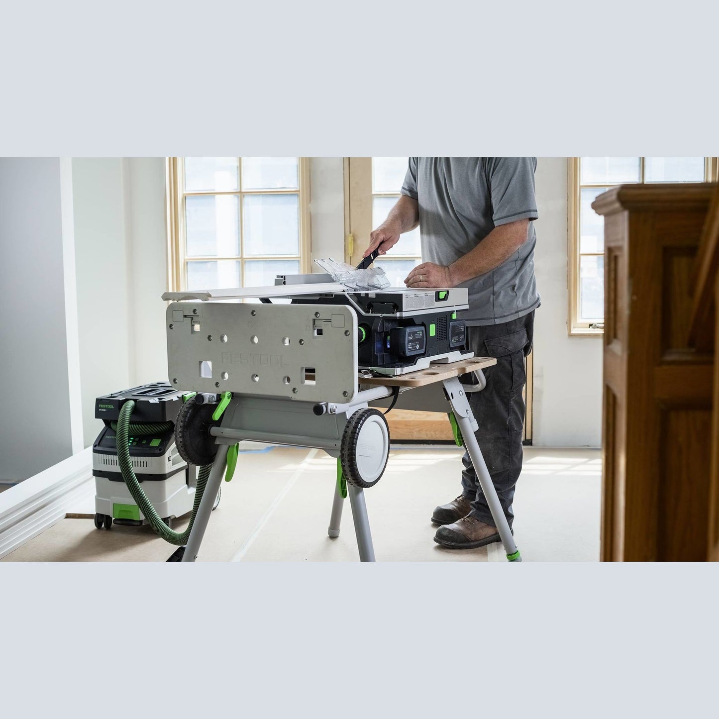 Person operating Festool cordless table saw on mobile stand with dust extraction in bright home improvement setting