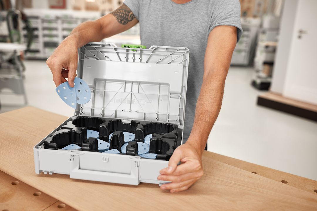 Person placing blue sanding abrasives into gray Festool Granat storage system for power tool accessories and sanding supplies