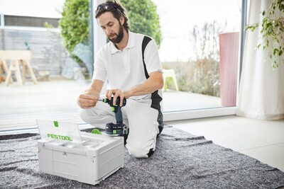 Man assembling drill bit onto Festool cordless drill next to branded case during home improvement task indoors