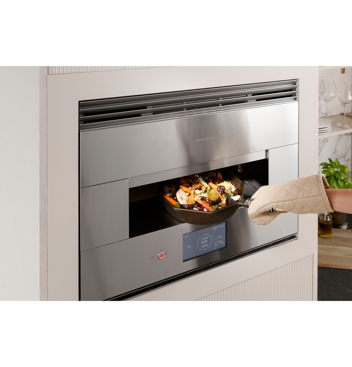 Contemporary stainless steel hearth oven built into wall with digital controls and person removing cooked food with oven mitt
