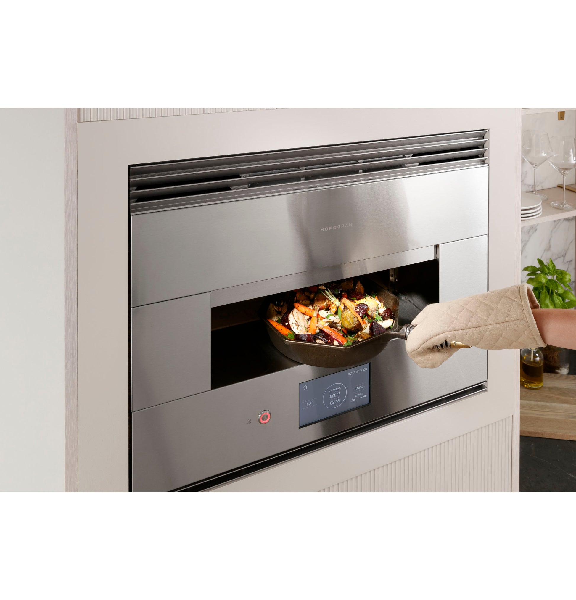 Contemporary stainless steel hearth oven built into wall with digital controls and person removing cooked food with oven mitt