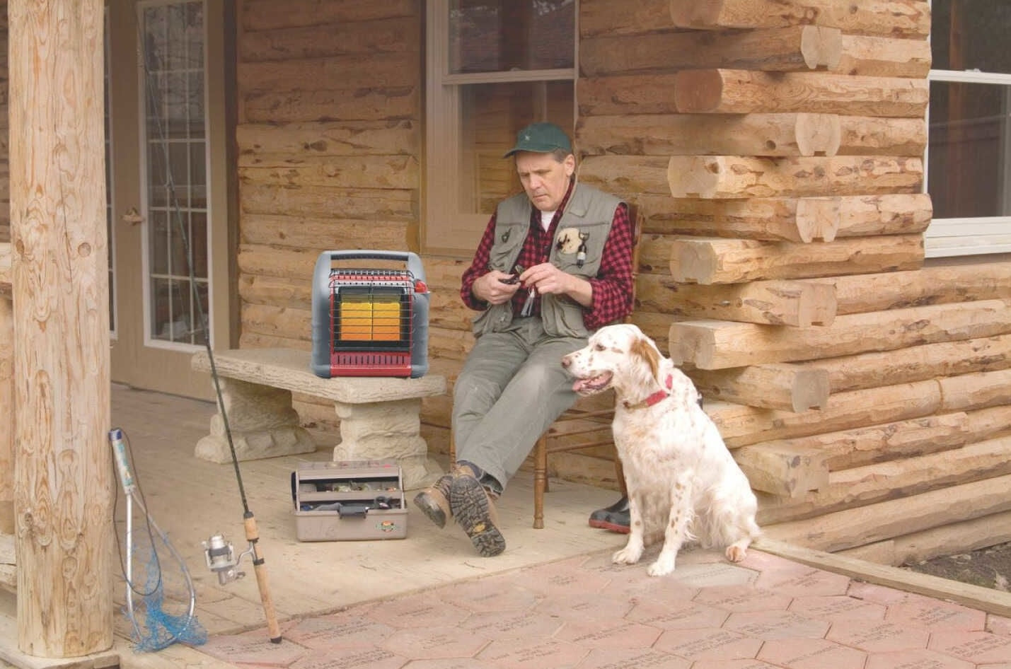 Man sitting on chair by log cabin porch with dog and portable radiant propane heater in All Products collection
