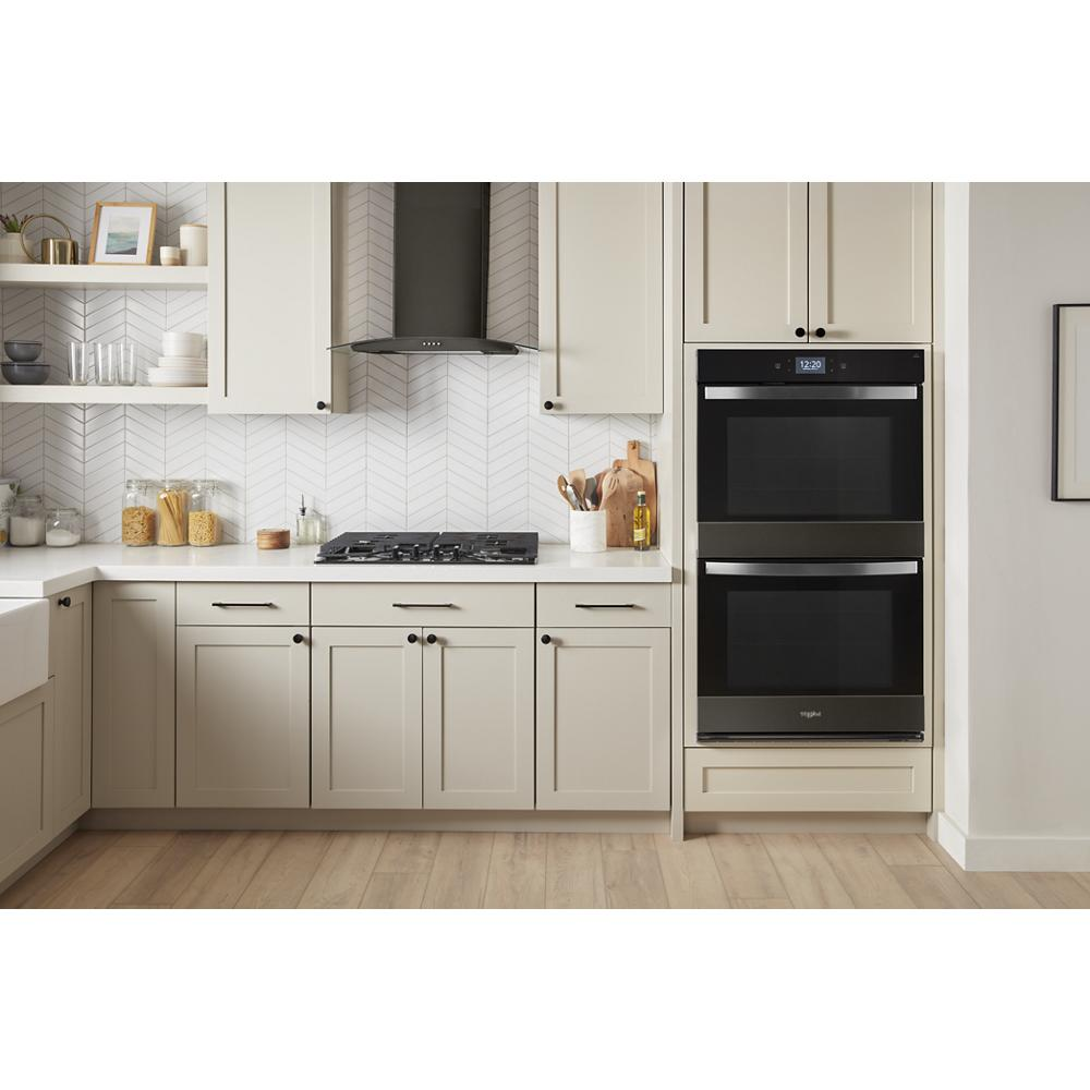 Modern kitchen featuring dual built-in ovens, gas cooktop, and a concave glass wall mount vent hood above countertop.