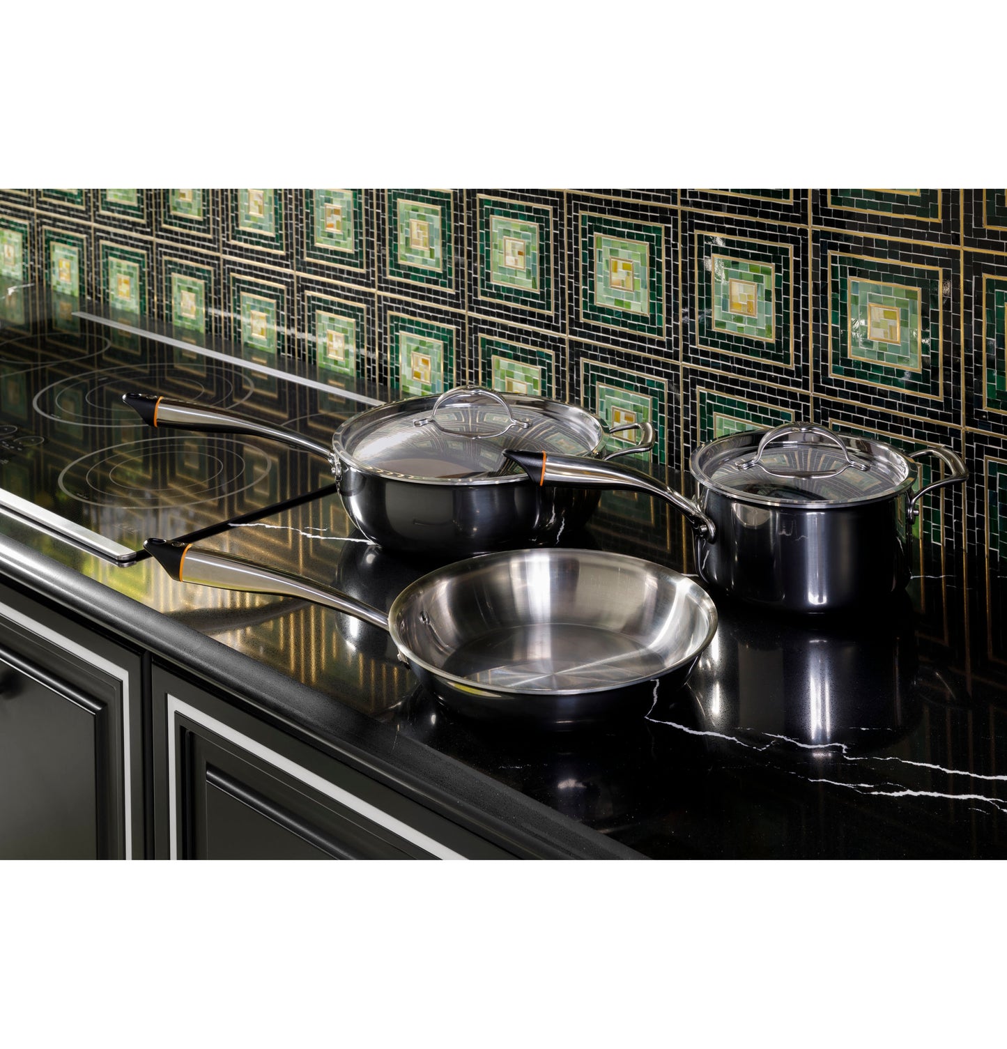 Black glass cooktop with three stainless steel pots and pans on a polished black marble countertop in modern kitchen