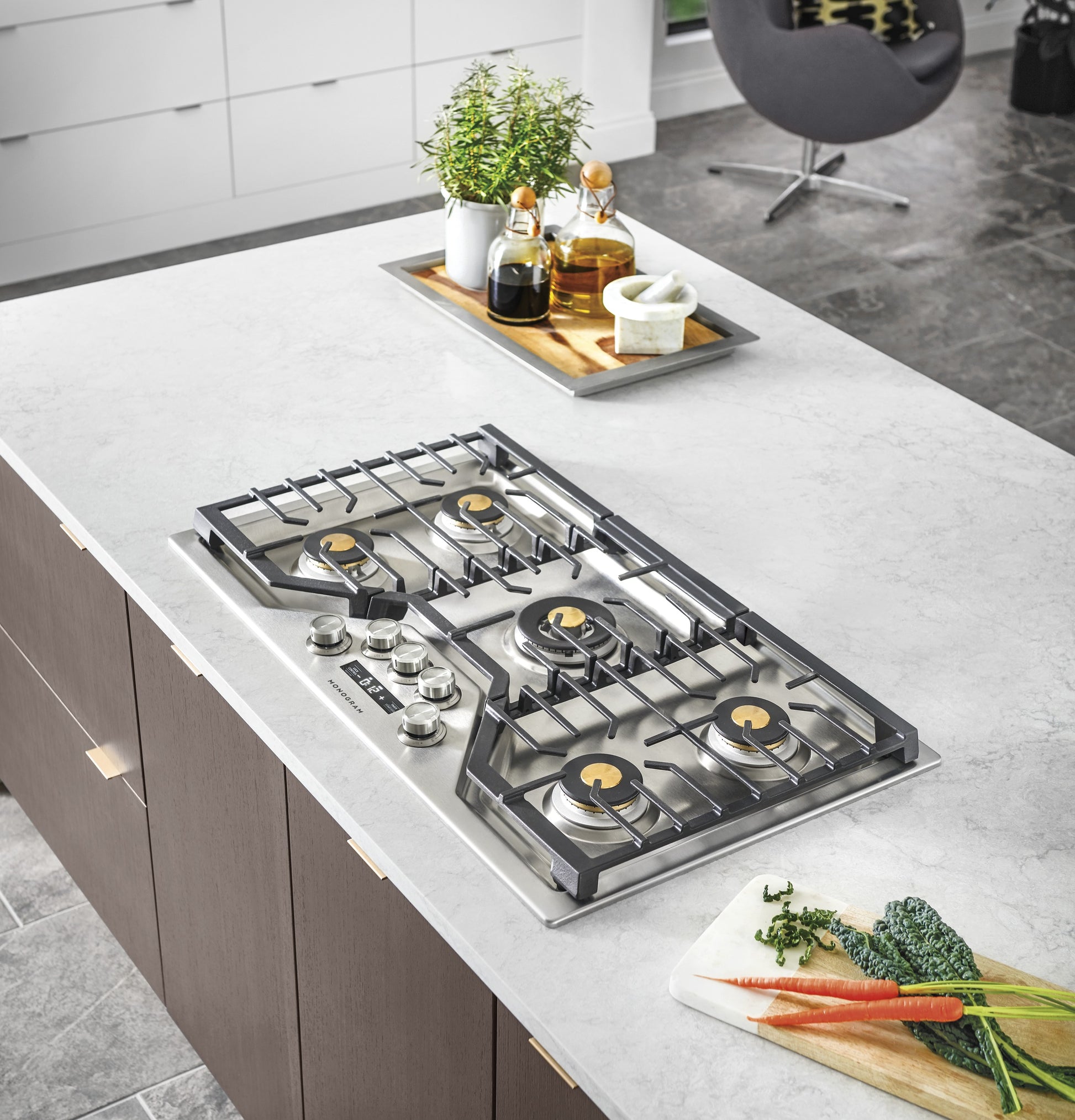 Modern stainless steel gas cooktop with brass burners and cast iron grates in contemporary kitchenware setting