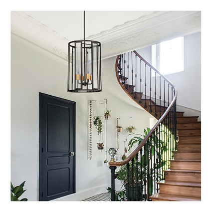 Modern black metal cage pendant light fixture hanging above wooden spiral staircase in a bright home interior