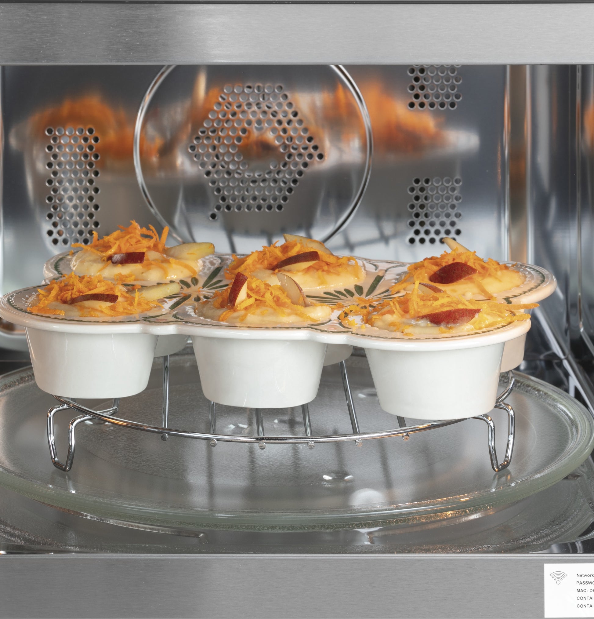 Four ramekins with baked cheesy and pepperoni-topped dish inside stainless steel countertop microwave oven