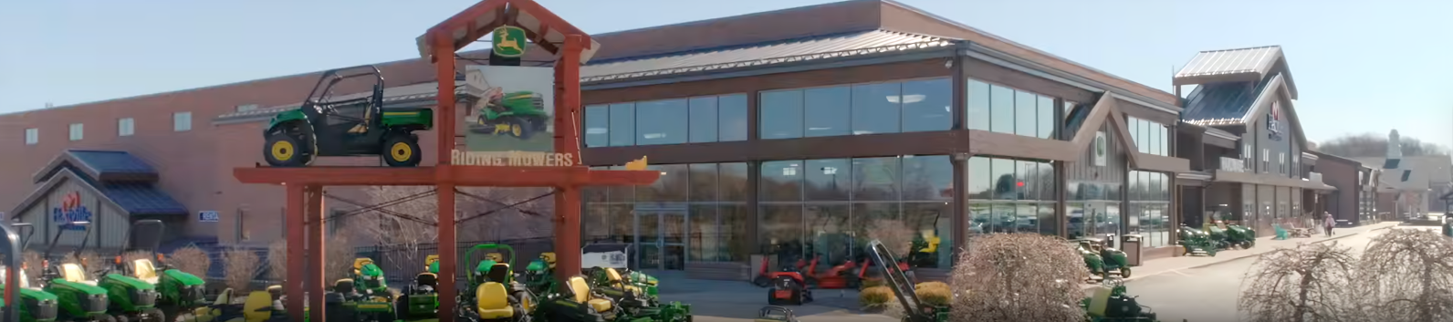 Exterior view of a large home improvement store featuring outdoor displays of green and yellow lawn tractors and utility vehicles under a clear sky.