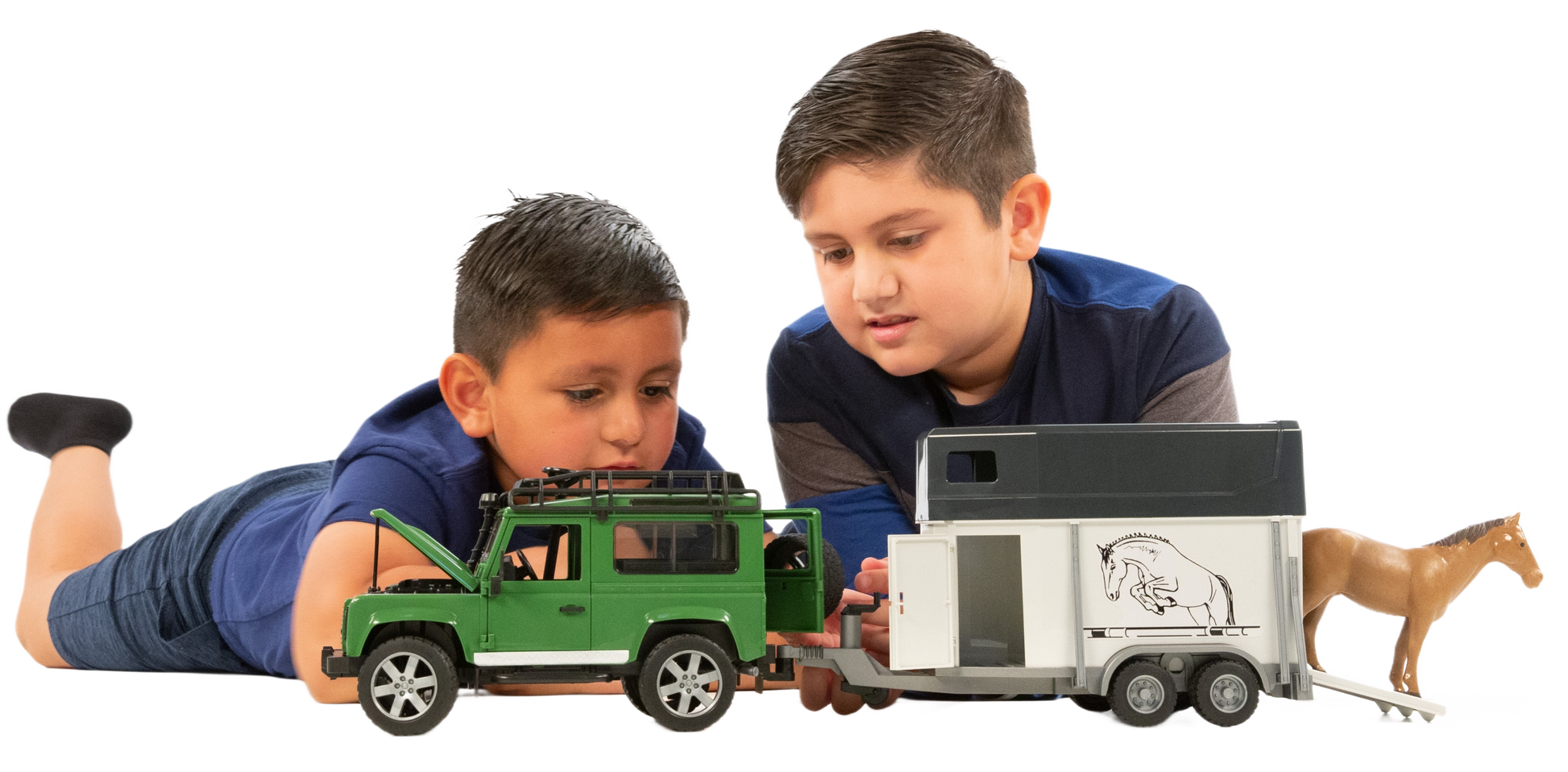 Two boys playing with a green Land Rover toy towing a white horse trailer with a brown horse figure inside