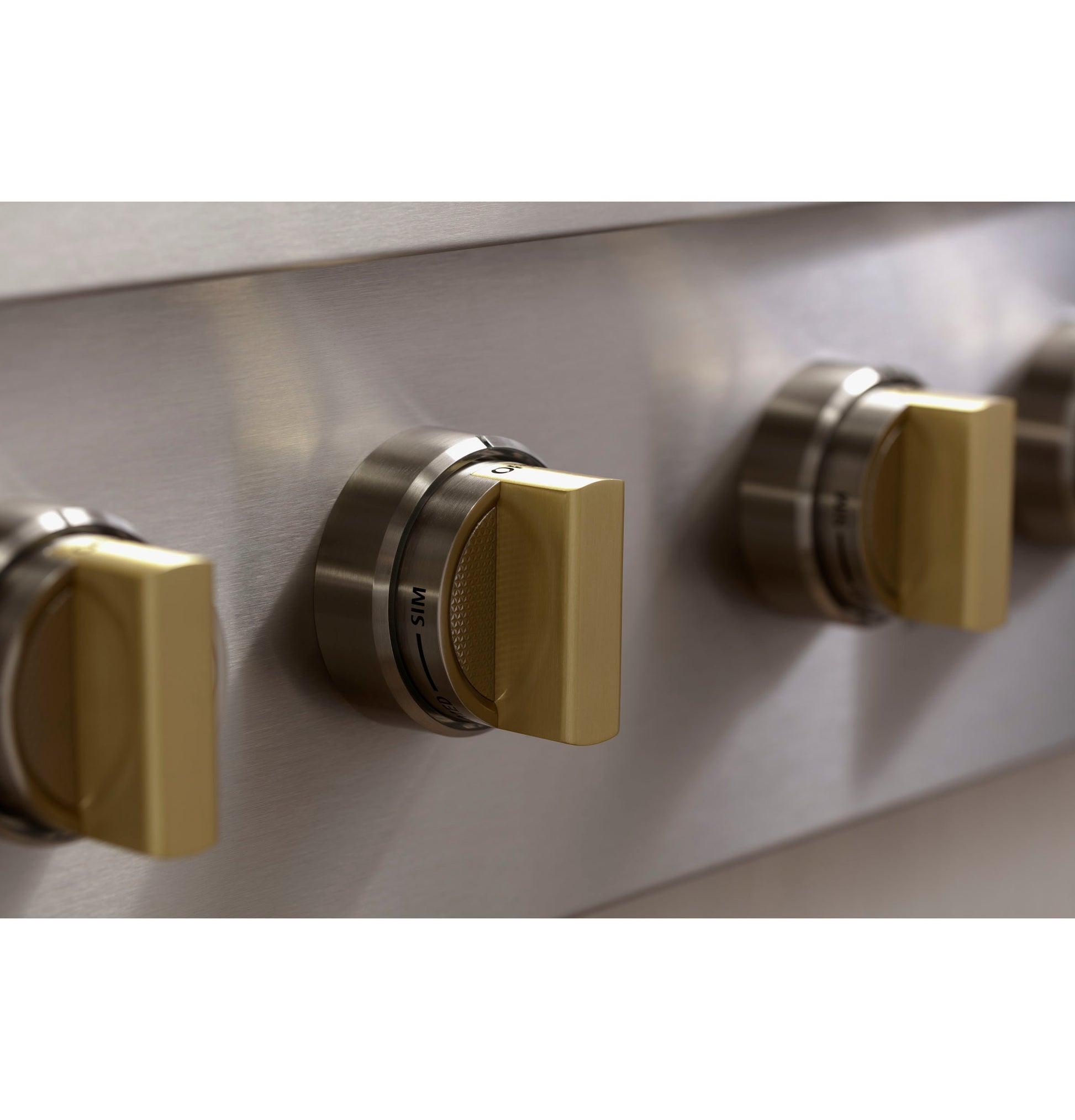 Close-up of brushed stainless steel gas rangetop control knobs with gold accents in kitchen appliances and cooktops collection