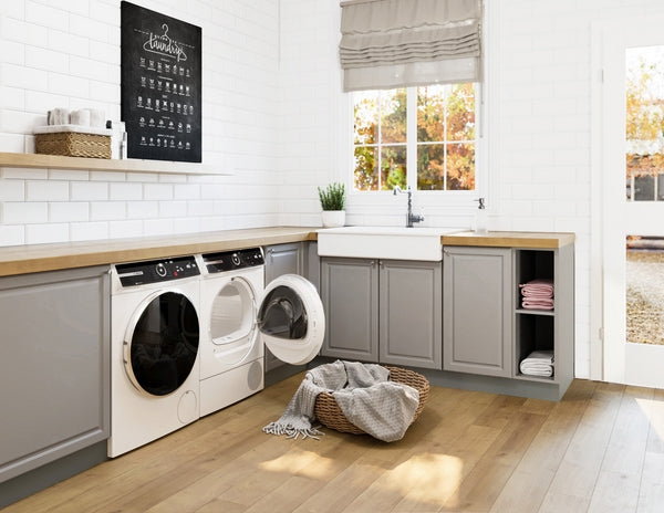 Modern laundry room with gray cabinetry, front load washer with open door, wood countertop, and farmhouse sink beneath window