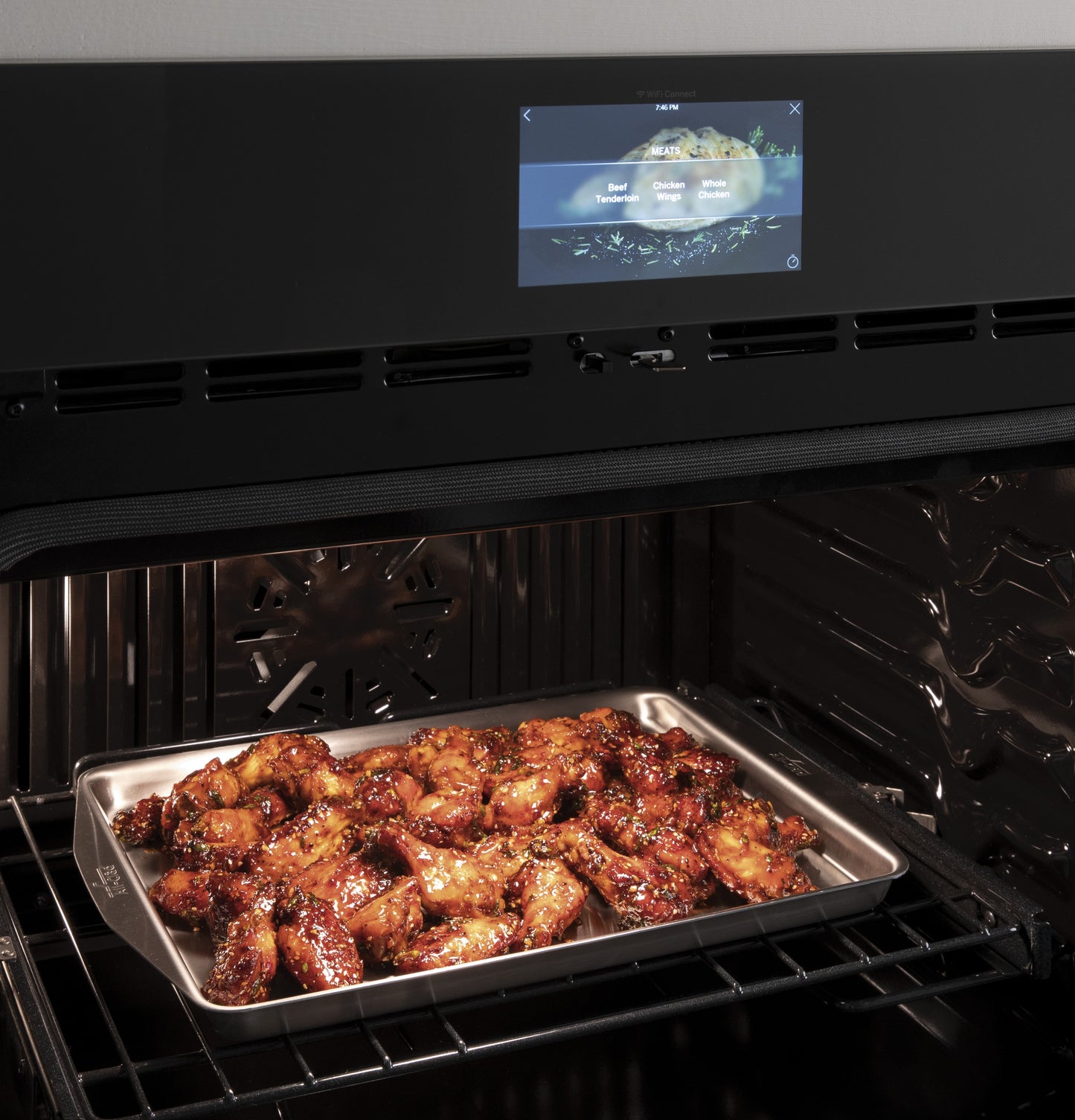 Tray of glazed chicken wings baking inside a modern smart convection double wall oven with touchscreen controls