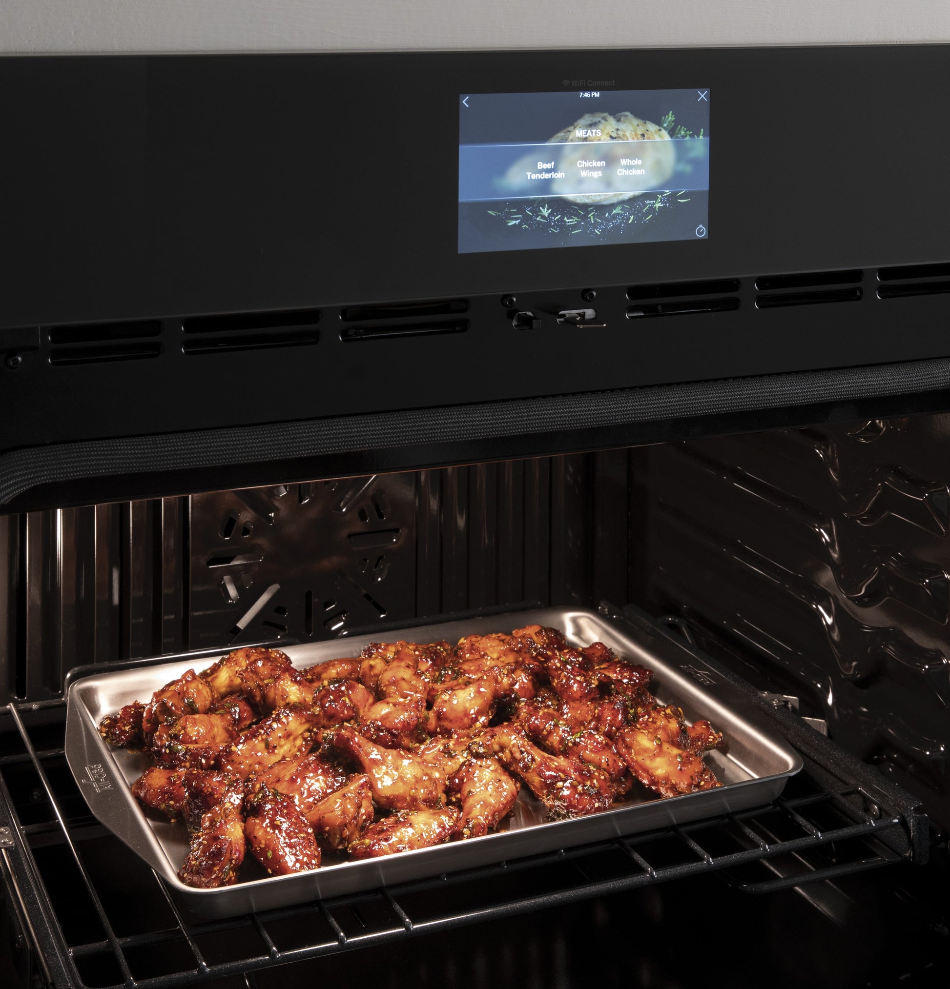 Tray of glazed chicken wings baking inside a modern smart convection double wall oven with touchscreen controls