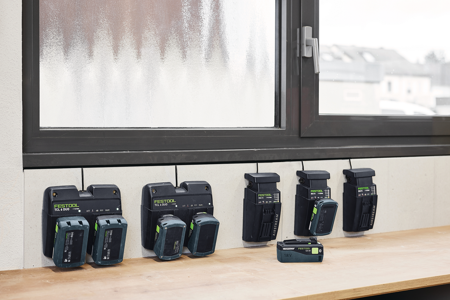 Festool 577328 Energy Set SYS 18V 2x8.0/2xSCA16 displaying multiple battery chargers and 18V batteries on a wooden surface near a window