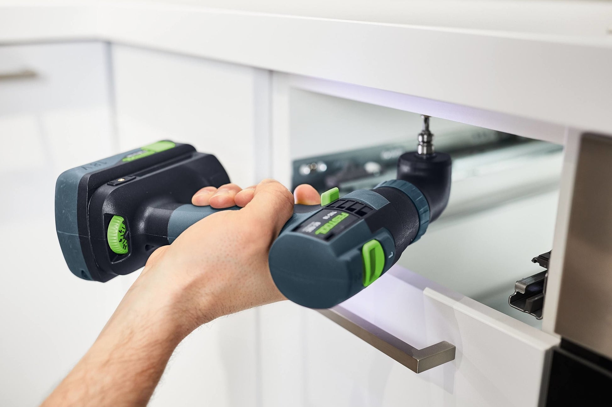 Compact cordless drill with green accents driving a screw into white wooden cabinetry for home improvement.