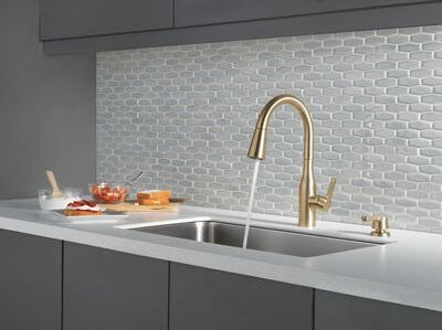 Single handle champagne bronze kitchen faucet with curved spout and matching soap dispenser in modern home improvement setting