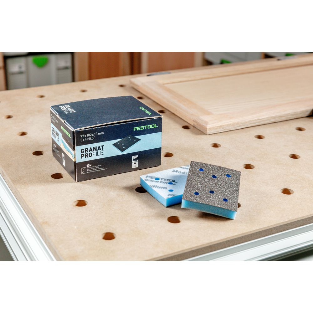 Box of Festool sanding pads with two blue abrasive sheets on perforated tool accessories workbench surface