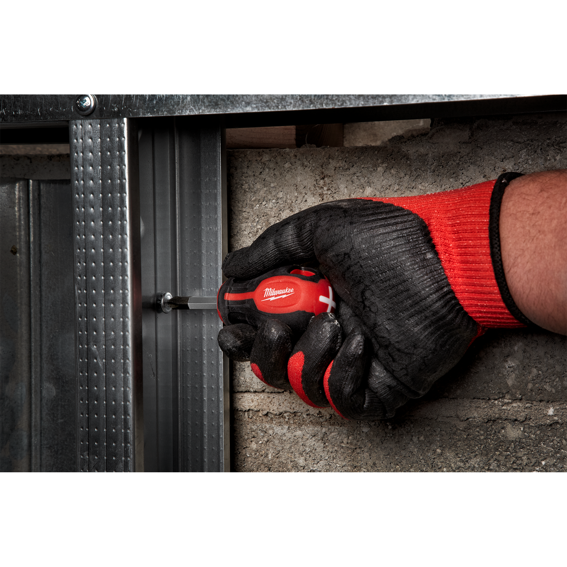 Hand with black and red glove using compact Milwaukee screwdriver to fasten metal frame in home improvement task