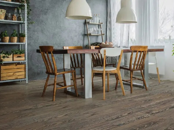 Dining area with a wooden table surrounded by mixed wooden chairs, large white pendant lights, a metal shelving unit with plants, and natural light from a window.