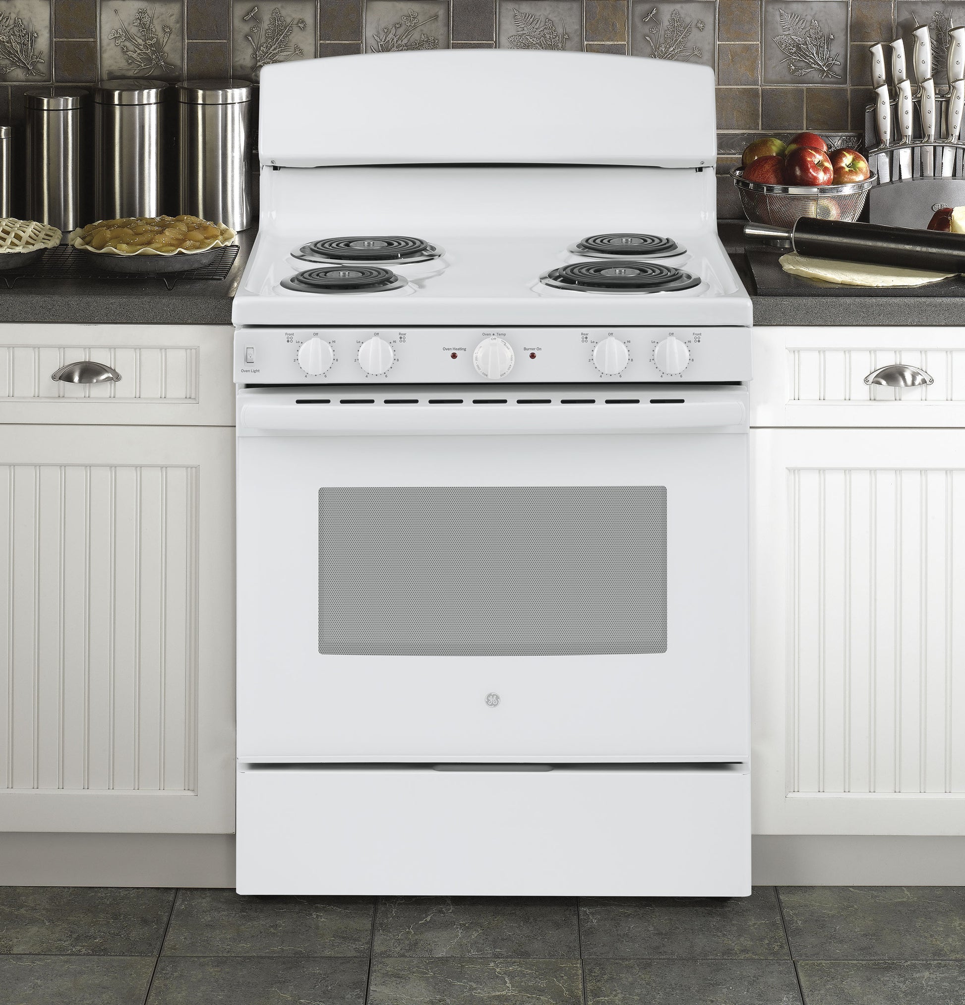 White free-standing electric range with four coil burners in a traditional kitchen setting with cabinetry and cooking accessories