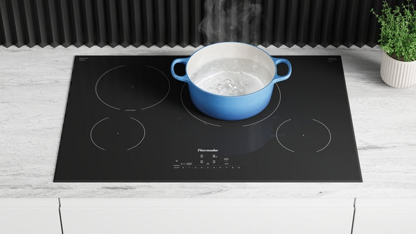 Black glass induction cooktop with four burners heating a blue pot of boiling water in modern kitchen setting