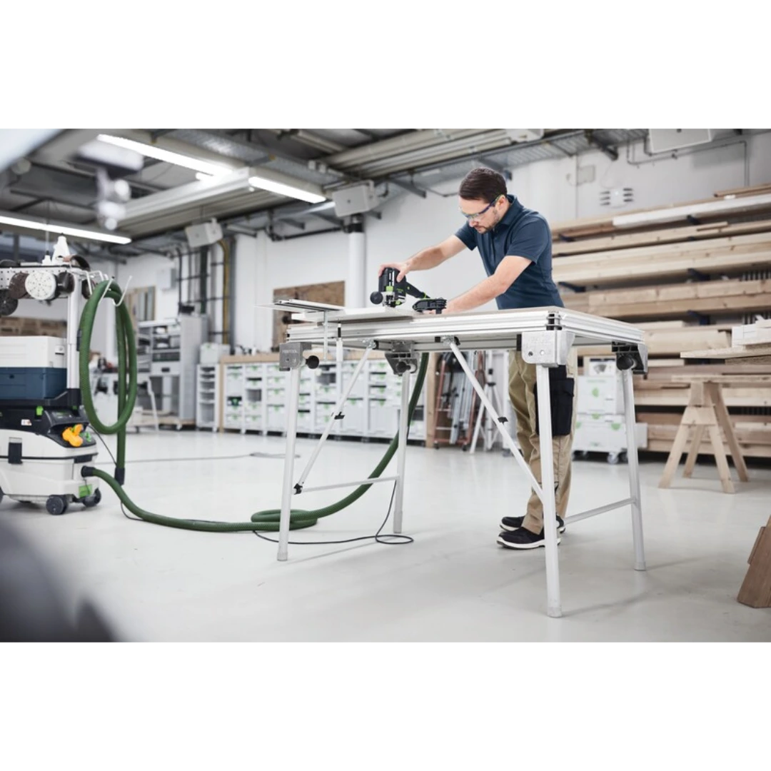Man using woodworking tool on multifunction table with attached dust extractor in workshop setting