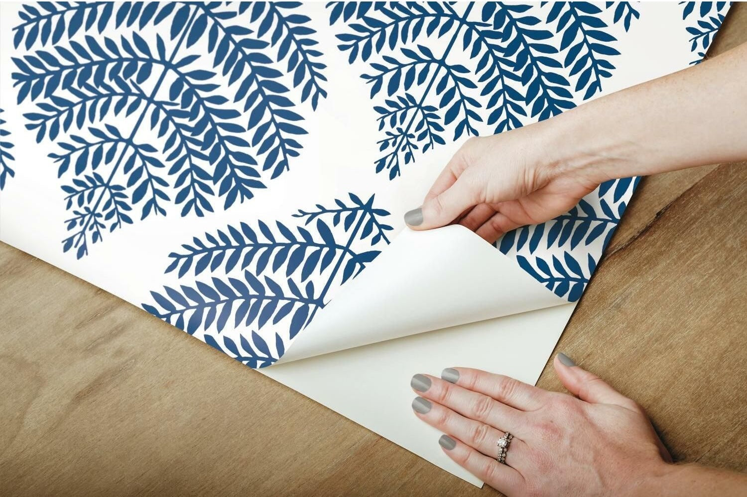 Hands peeling blue fern pattern peel and stick wallpaper from white vinyl sheet for home decor