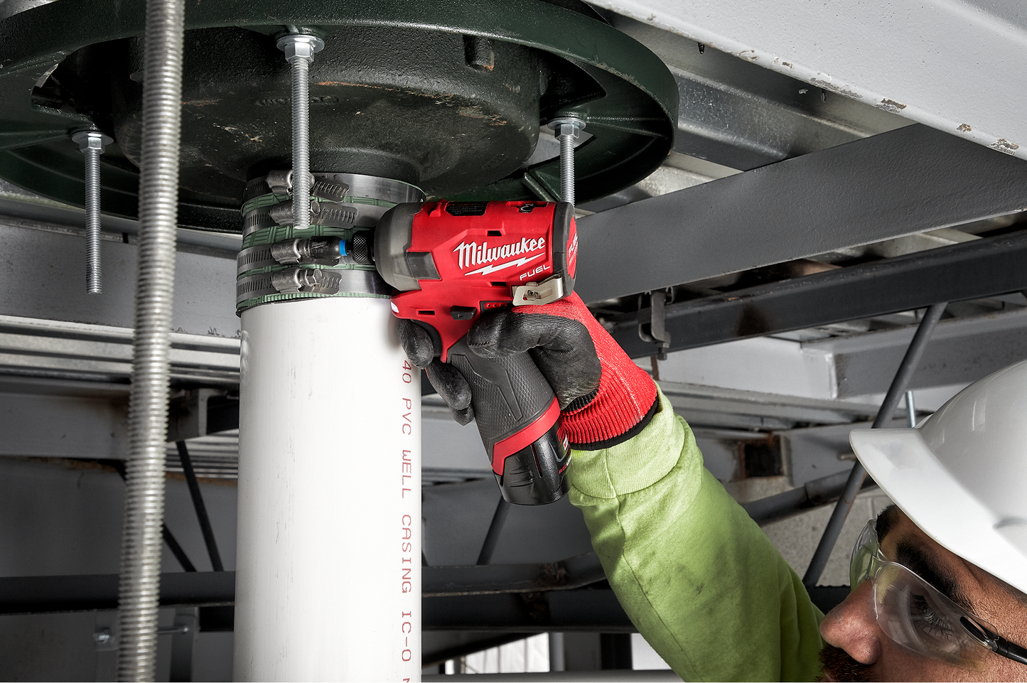 Technician using a red Milwaukee M12 hydraulic driver on PVC pipe under building structure in tools collection