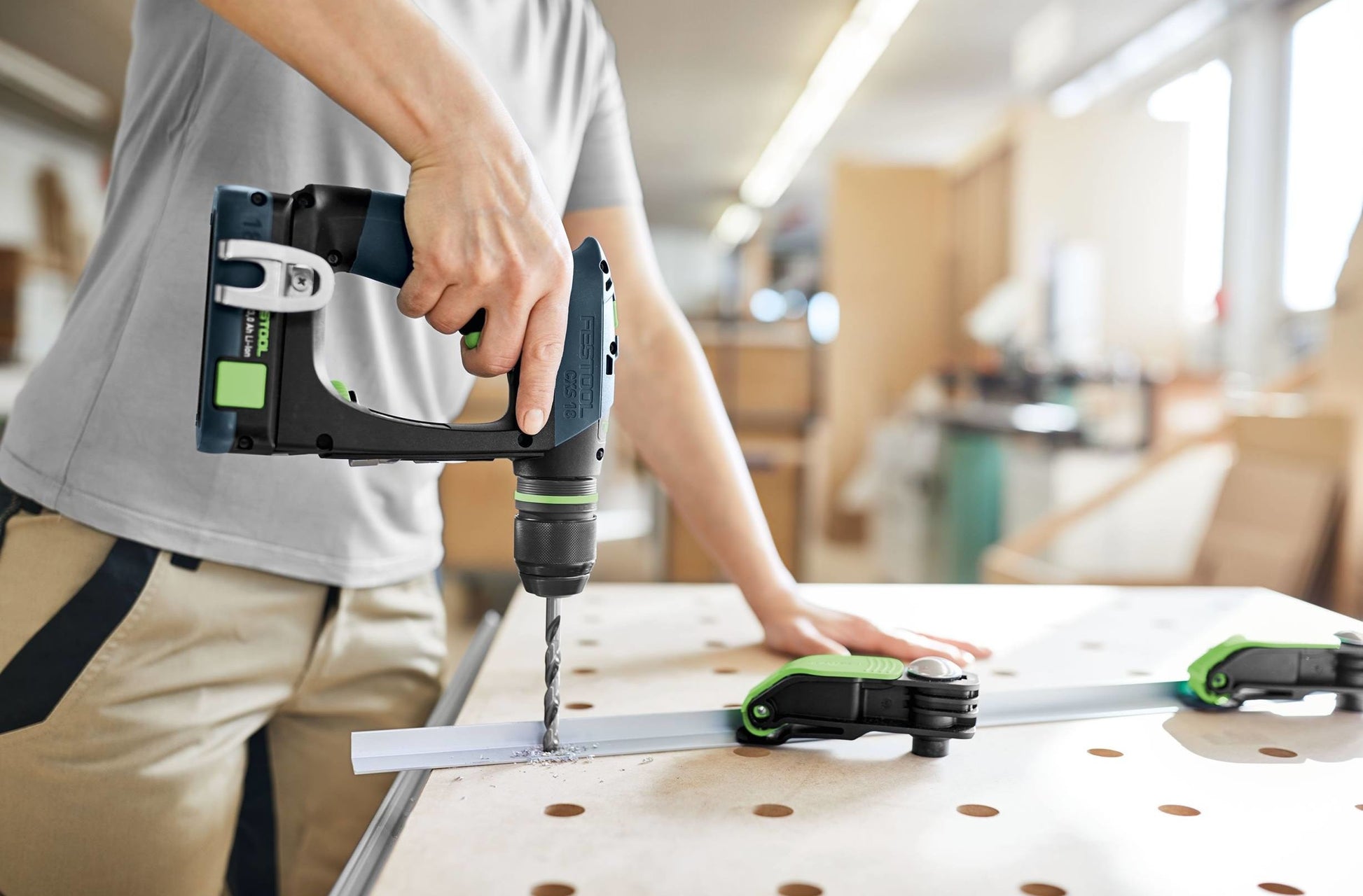 Person using cordless drill on wood with guide clamp in bright woodworking workshop environment