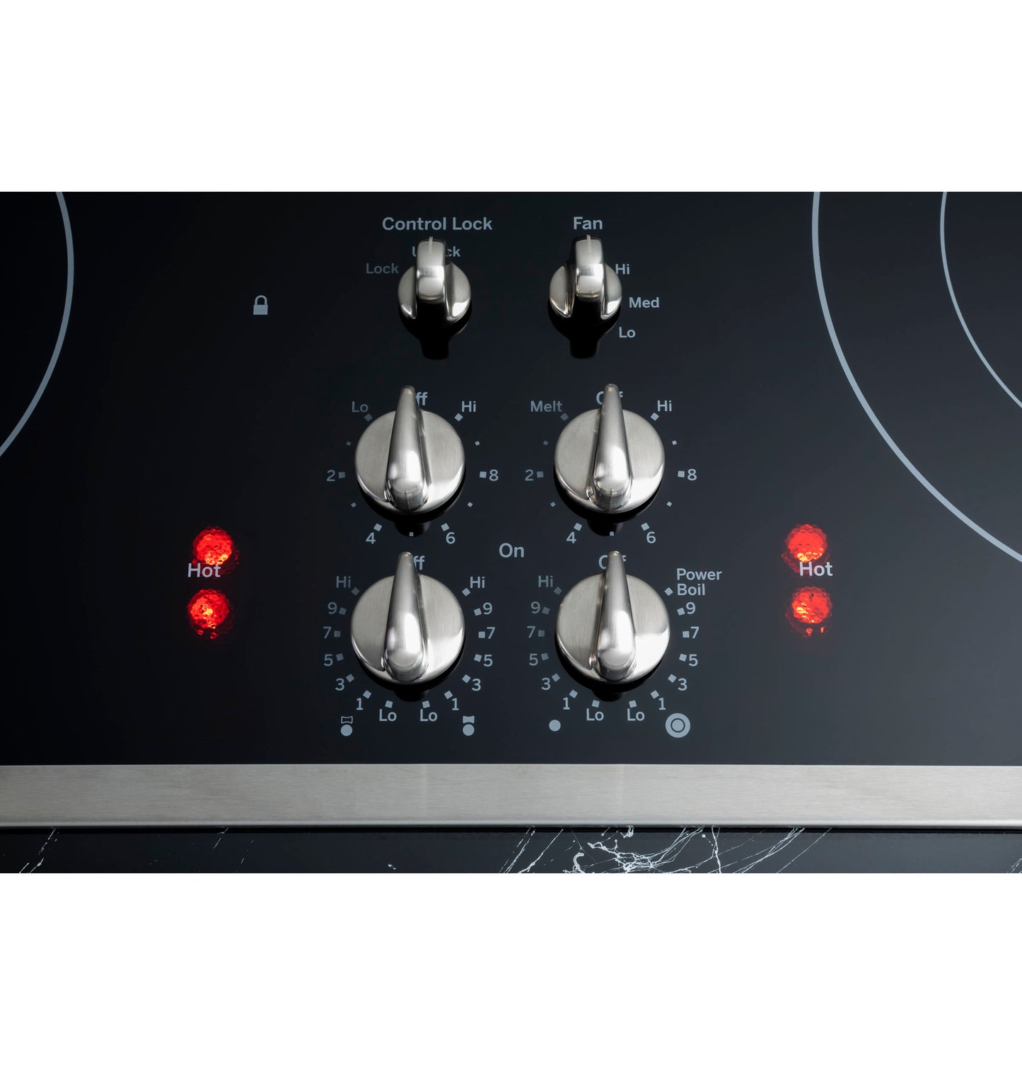 Close-up of stainless steel control knobs with illuminated hot indicators on black glass downdraft cooktop panel