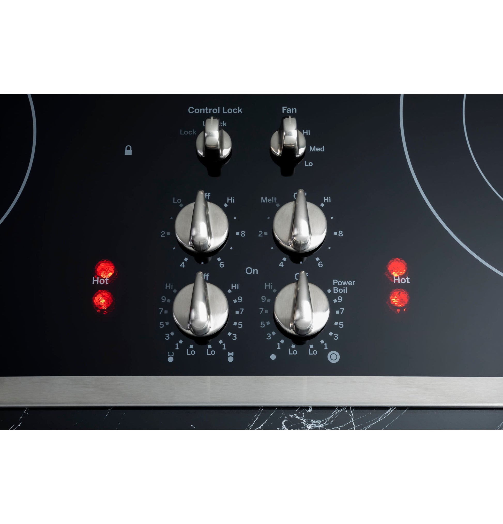 Close-up of stainless steel control knobs with illuminated hot indicators on black glass downdraft cooktop panel