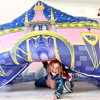 Child playing inside a colorful inflatable royal castle fort with blue, pink, and yellow design for indoor fun