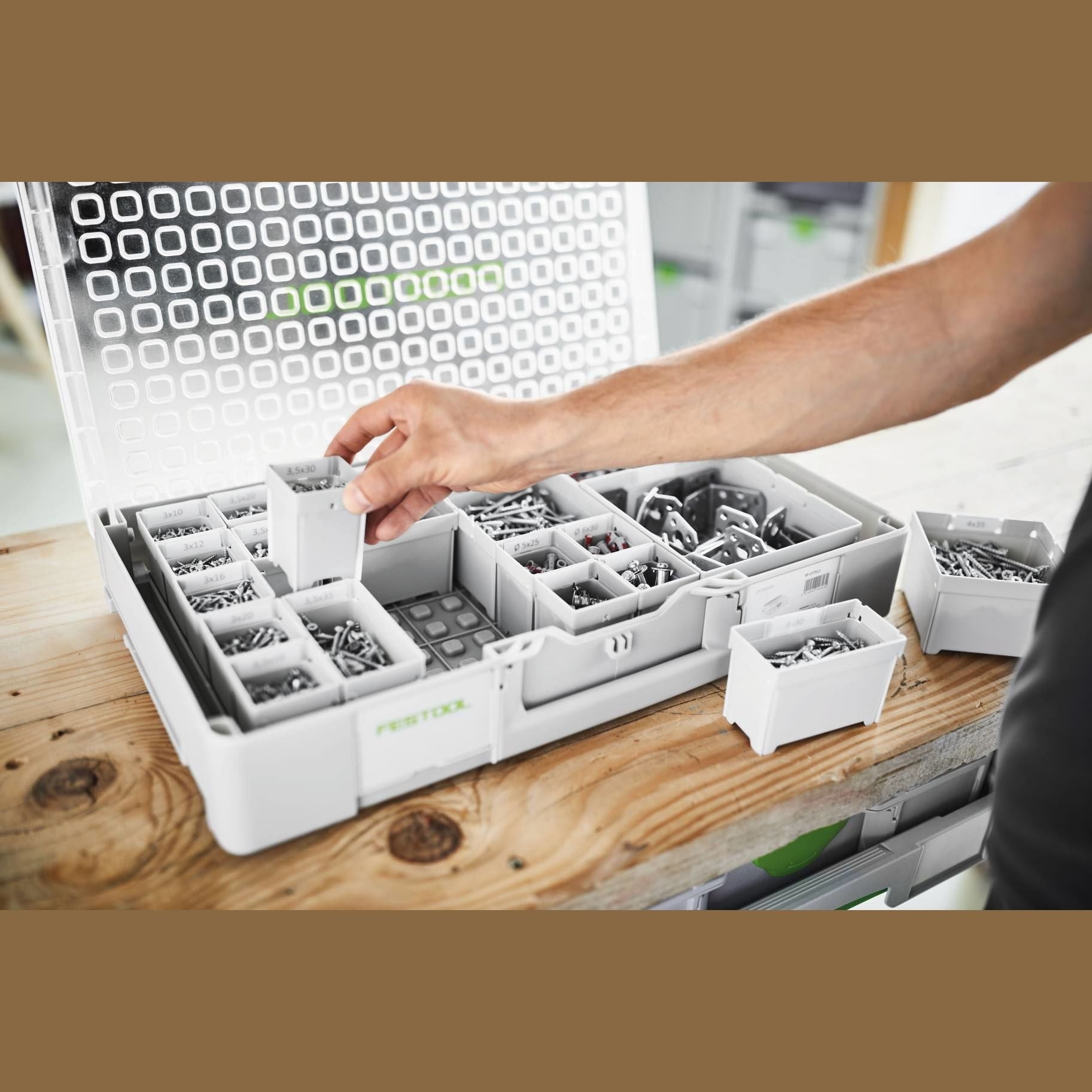 Hand organizing small screws and hardware in clear-lidded modular plastic storage container for workshop organization