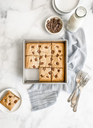 Square metal cake pan with freshly baked chocolate chip blondies and serving utensils in kitchenware collections