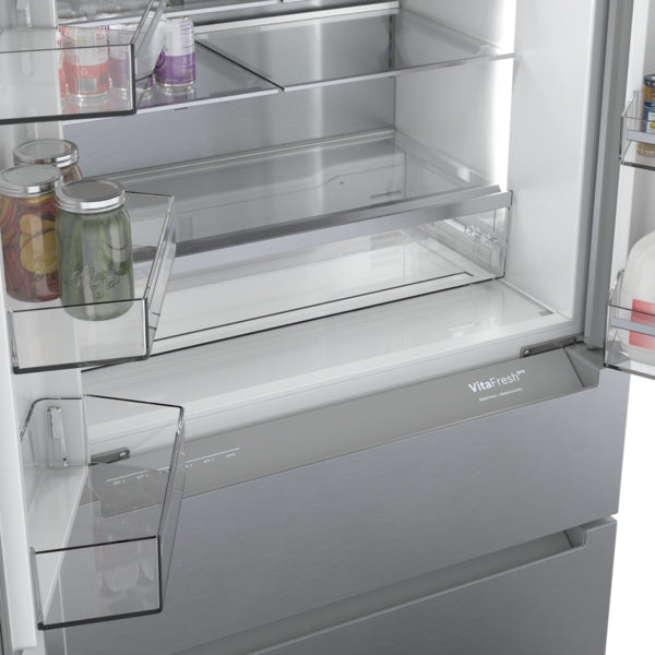 Open stainless steel French door refrigerator with clear shelves and VitaFresh storage drawer in modern kitchen appliances collection
