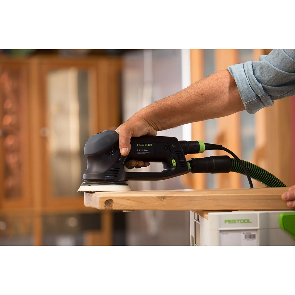 Person using Festool dual mode sander with dust extraction hose smoothing wooden surface for home improvement task