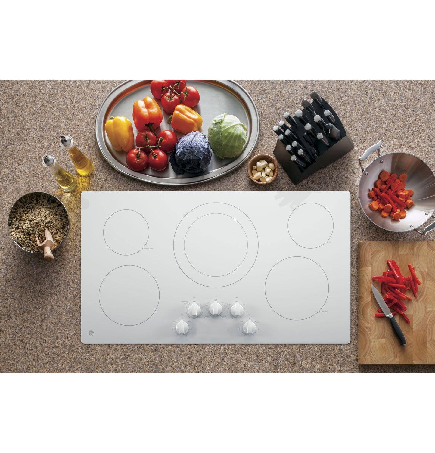 White built-in electric cooktop with five knob controls surrounded by fresh vegetables and kitchen tools for home improvement