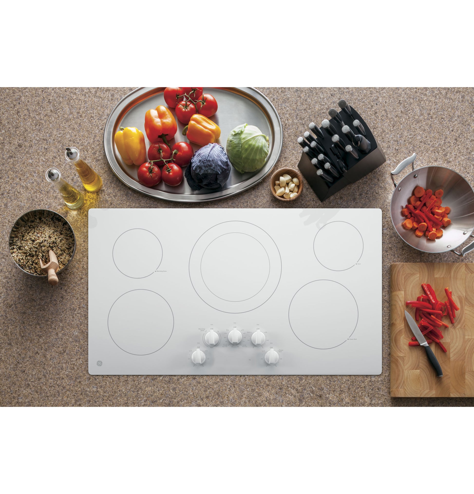 White built-in electric cooktop with five knob controls surrounded by fresh vegetables and kitchen tools for home improvement
