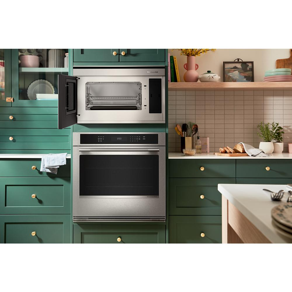 Built-in stainless steel convection microwave oven and wall oven in green kitchen cabinetry with brass knobs and countertop decor